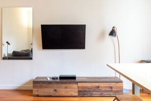 A minimalist living room with a flat-screen TV mounted on the wall, a wooden coffee table with drawers, a modern floor lamp, and a sofa. - Central and Bright 1BDR Apartment near Notre Dame (Paris)