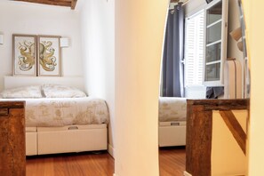 A bedroom with a bed, a nightstand, a window with shutters, and a wall-mounted lamp. - Central and Bright 1BDR Apartment near Notre Dame (Paris)