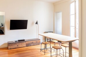 Una habitación moderna con televisión de pantalla plana en la pared, un escritorio con dos taburetes y un ventanal que proporciona luz natural.