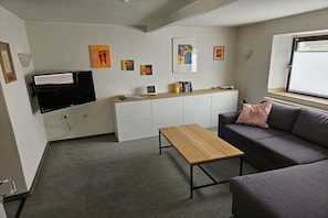 A modern living room with a sofa, a wooden coffee table, and a television mounted on the wall. - Holiday home in Welling with Wi-Fi (Welling)