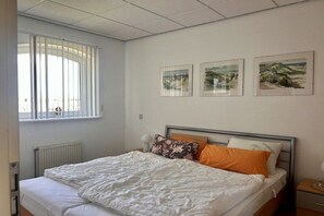 Ein Schlafzimmer mit einem Bett, einem Fenster mit Jalousien und drei Wandbildern.