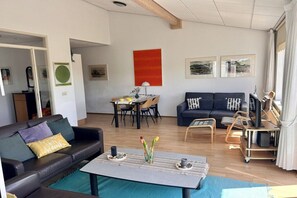 A living room with a sofa, a coffee table, and a dining area with chairs and a table. - Holiday apartment with 2 bedrooms (Julianadorp)