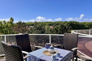Eine Terrasse mit Korbstühlen und einem für Tee gedeckten Tisch, mit Blick auf ein bewaldetes Gebiet.