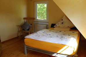 A single bed with a yellow mattress and floral bedding in a room with wooden flooring and a window. - Holiday apartment with 1 bedroom (Rüdesheim)
