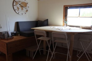 Een knus woongedeelte met een kitchenette, een eettafel met stoelen, een bank en een wereldkaartklok.
