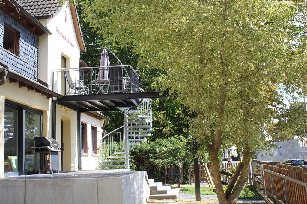 Ein Wohngebäude mit Balkon, Treppe und einem Baum im Hintergrund.