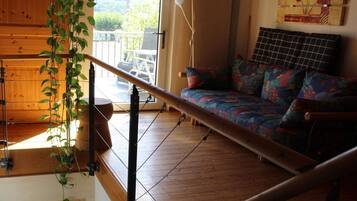 Ein Zimmer mit Holzboden, einem farbenfrohen Sofa, einer hängenden Pflanze und Blick durch ein Fenster.