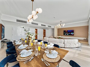 A modern dining area with a wooden table set for a meal, a sofa, and a TV mounted on the wall. - Kensington Superlex Penthouse Burj Views (Dubai)