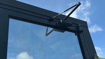 A window with a wiper mechanism, clear sky, and reflections of trees and clouds.