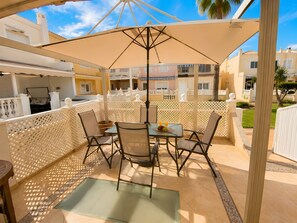 An outdoor patio area with a table and chairs, a pergola providing shade, and a view of neighboring buildings. - Holiday Home 'Almerimar Golf Spacious Duplex Near' with Shared Pool, Wi-Fi and Air Conditioning (El Ejido)