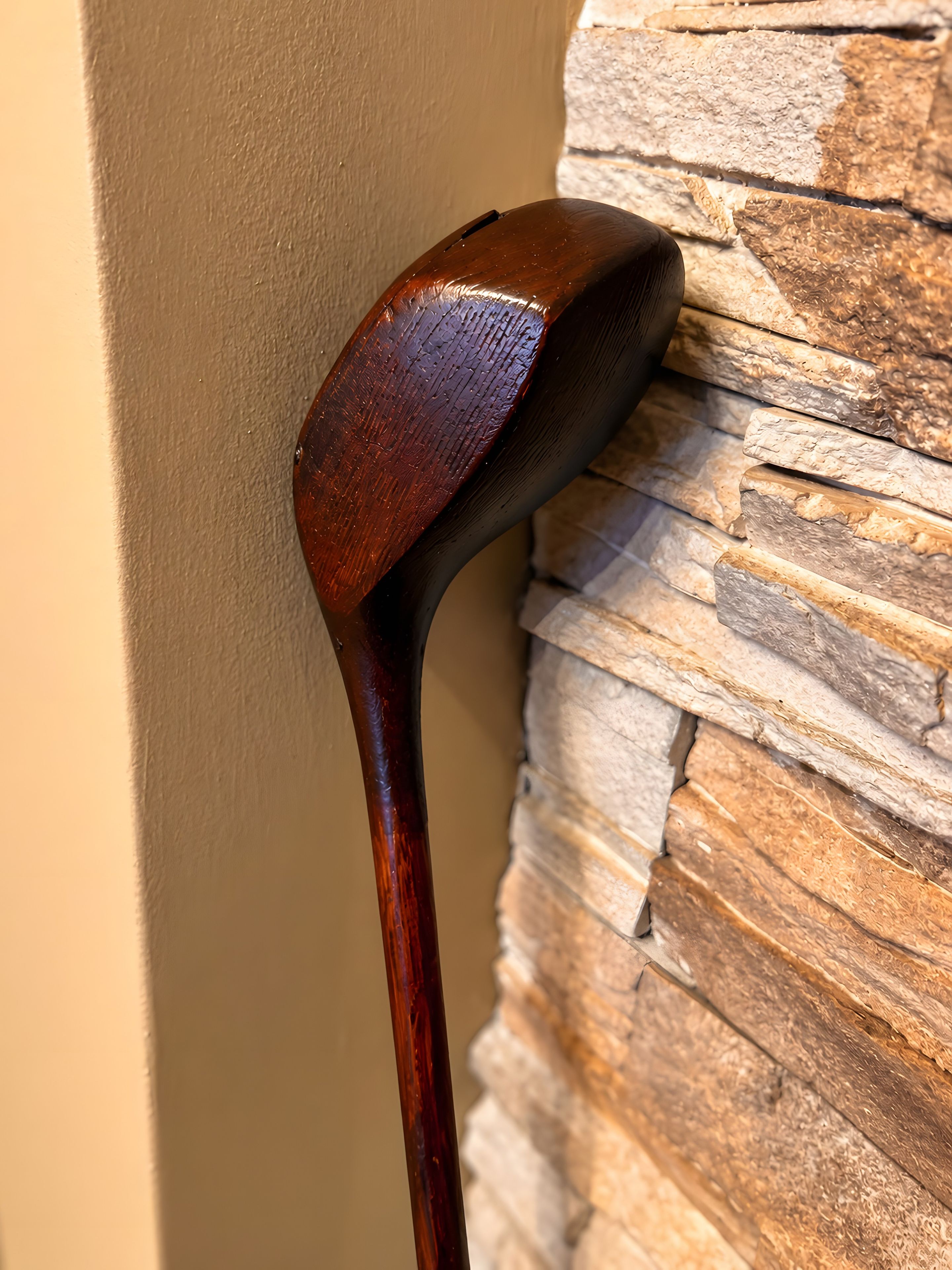 Un bastone da passeggio in legno appoggiato a un muro dalla superficie irregolare.