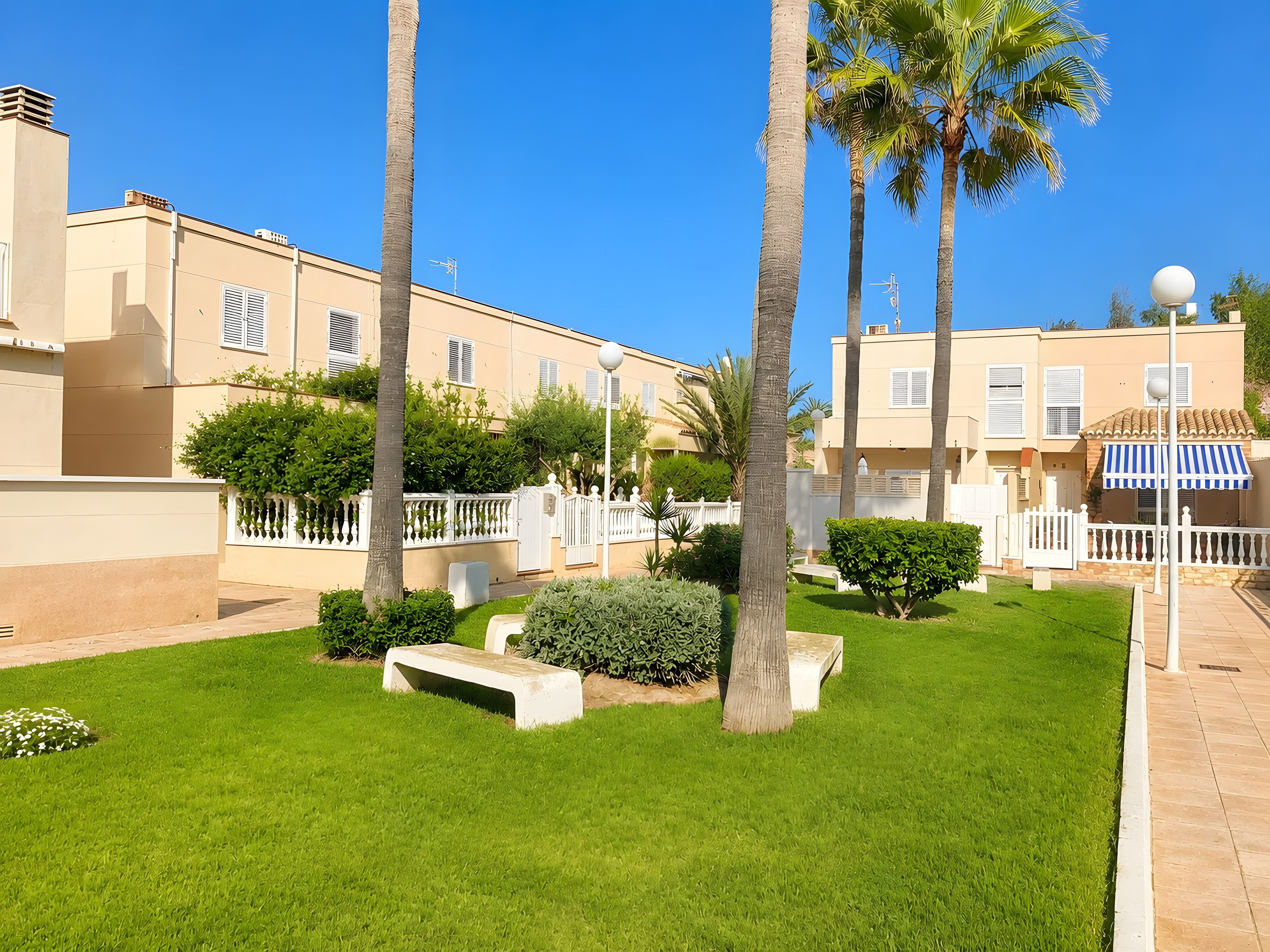 A residential area with a well-maintained lawn, palm trees, and a building with balconies.