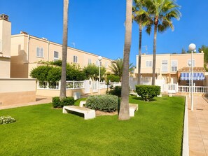 A residential area with a well-maintained lawn, palm trees, and a building with balconies. - Holiday Home 'Almerimar Golf Spacious Duplex Near' with Shared Pool, Wi-Fi and Air Conditioning (El Ejido)