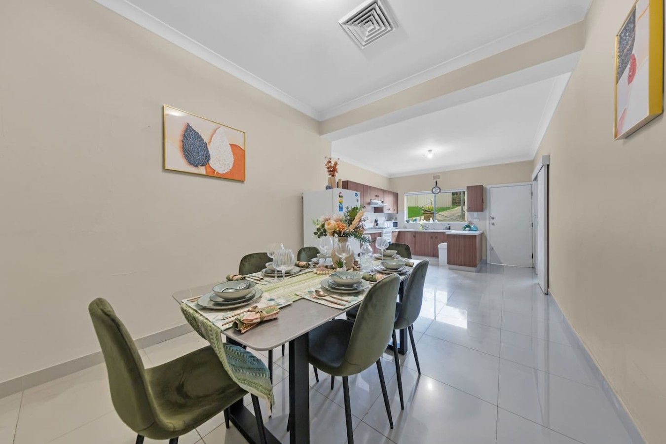 Un comedor con una mesa preparada para cuatro, sillas y una cocina al fondo.