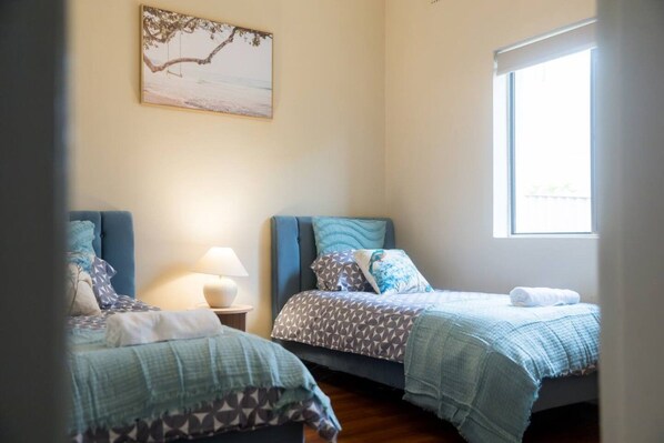 A room with two beds, a nightstand with a lamp, a painting on the wall, and a window.