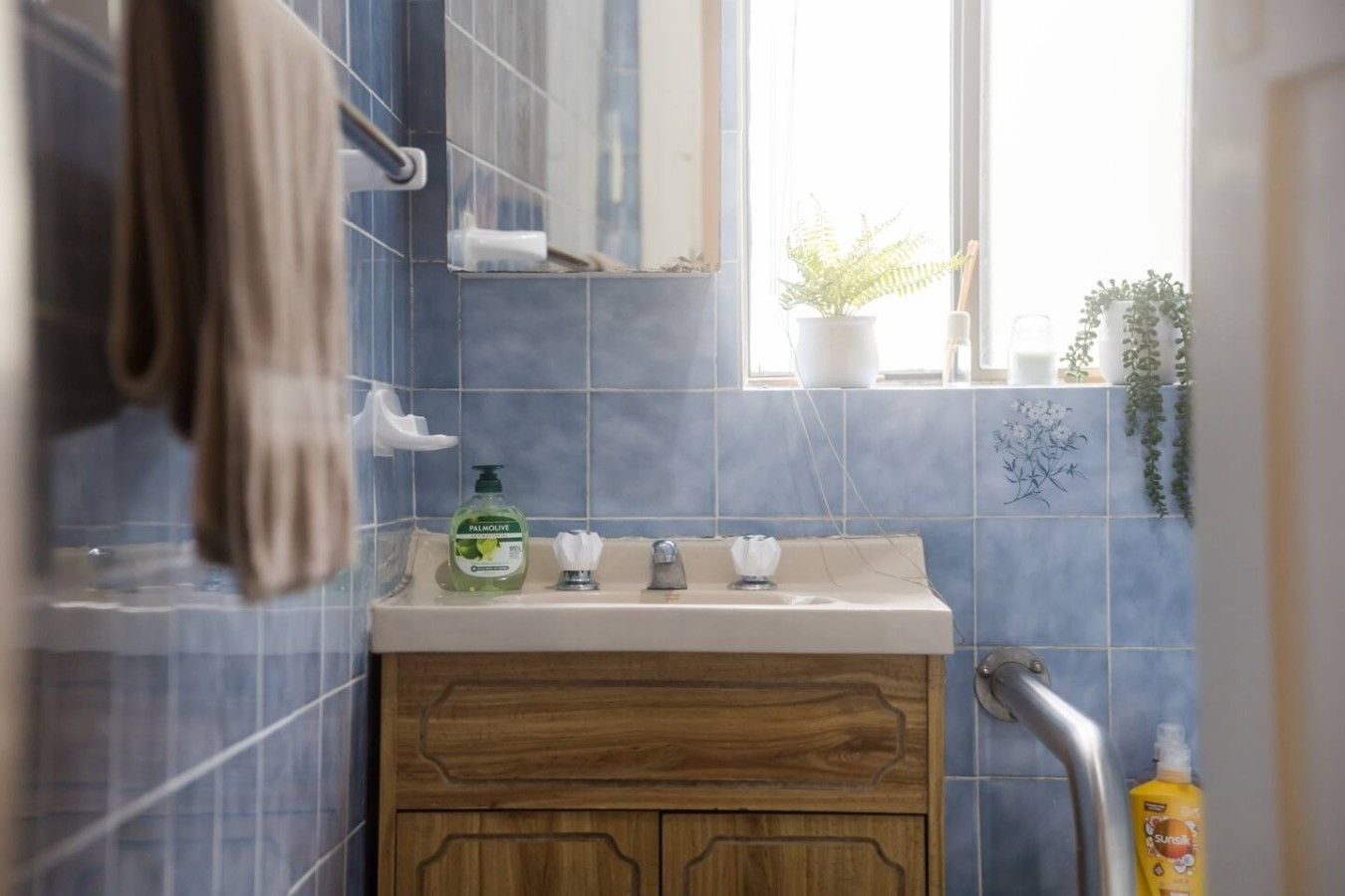 Un baño con tocador de madera, un espejo, una ventana con plantas y una toalla colgada en la pared.