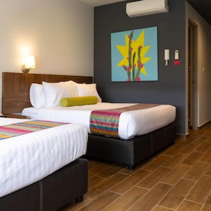 A hotel room with two beds, a wooden headboard, a wall-mounted air conditioner, a colorful artwork, and a telephone. - Estancias Vive MX el Marques (El Marques)