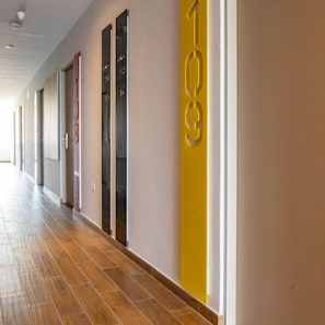 A hallway with numbered doors, wooden flooring, and a neutral color scheme. - Estancias Vive MX el Marques (El Marques)