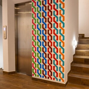 A vertical patterned wall with a metallic elevator door and a staircase with wooden steps. - Estancias Vive MX el Marques (El Marques)