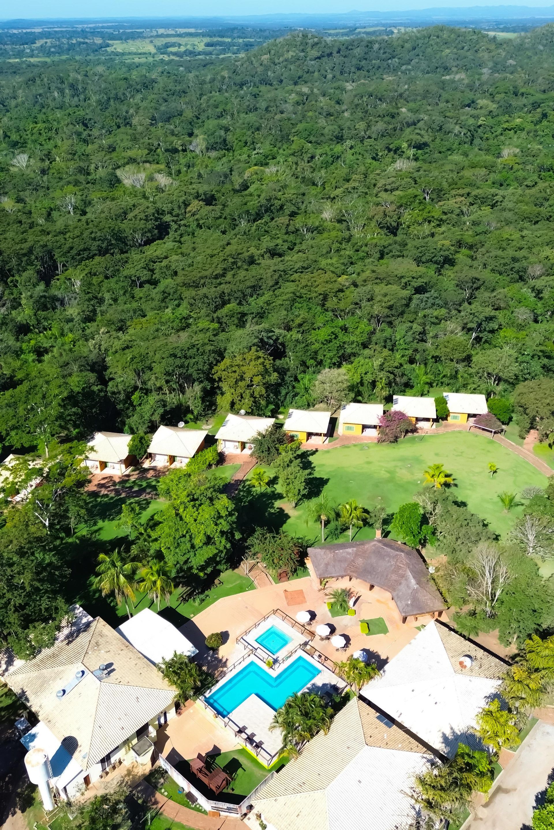 A resort with multiple buildings, a swimming pool, and a lush green landscape.