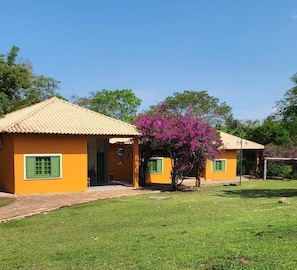 A small, single-story building with a tiled roof and green shutters, surrounded by a well-maintained lawn and a flowering tree. - Hotel Fazenda Cachoeira Serra da Bodoquena (Bodoquena)
