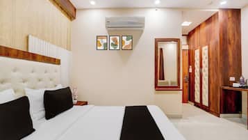 A hotel room with a large bed, a wooden wardrobe, a mirror, and an air conditioning unit.