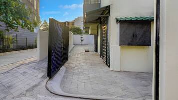 A narrow alleyway with a gated entrance, a tiled pathway, and a building with a green awning.