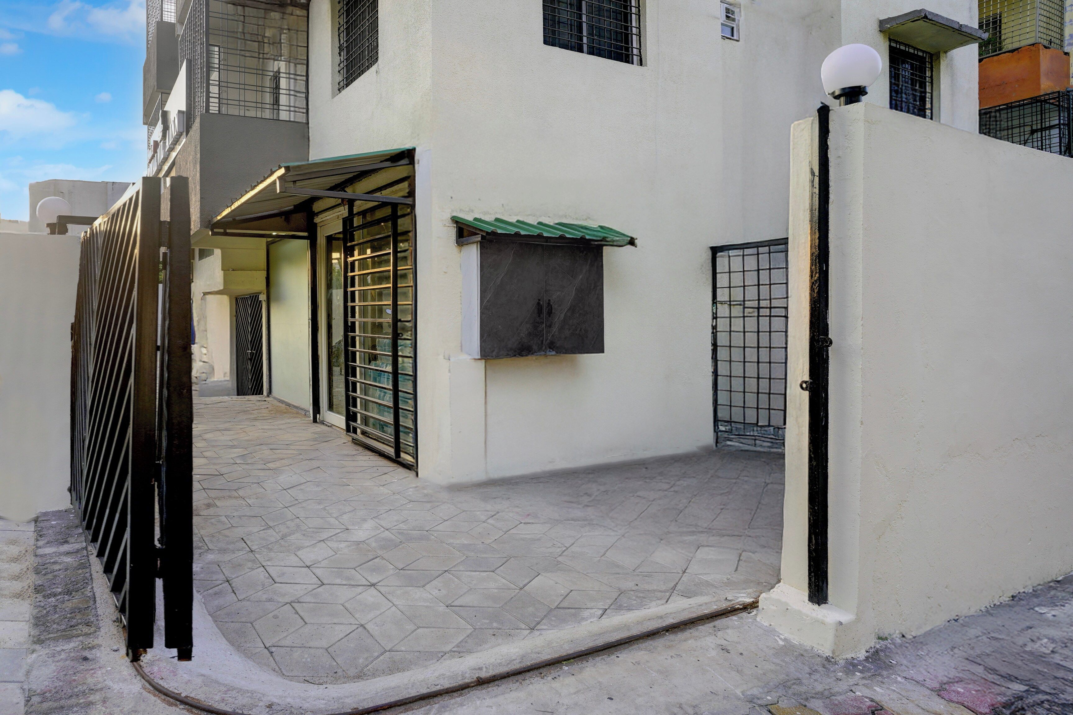 A gated residential area with a paved walkway, a metal gate, and a building with a green roof.
