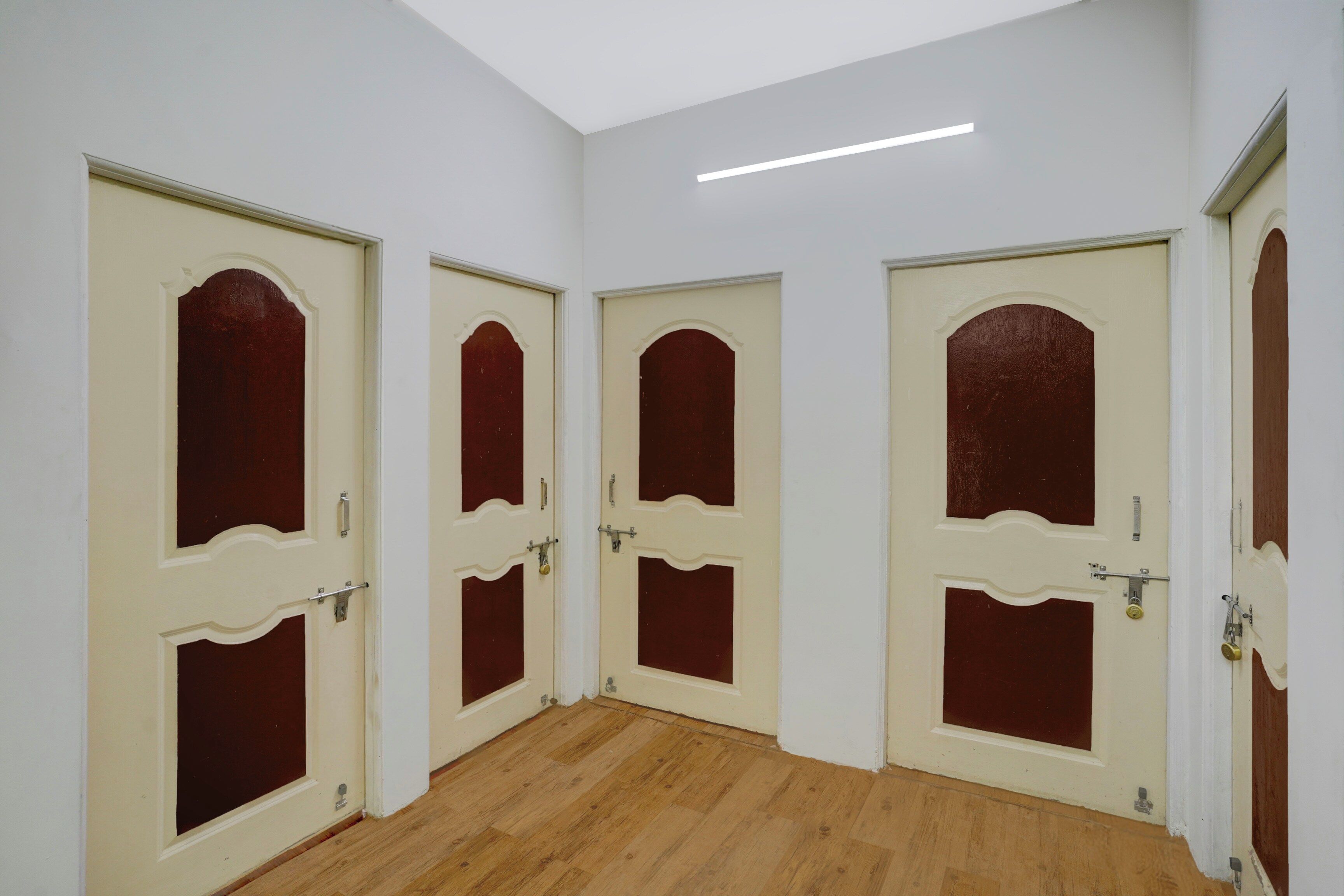 A hallway with four doors, each with a white frame and a red panel, leading to separate rooms. The floor is wooden, and the walls are painted white.