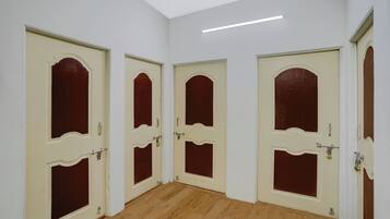 A hallway with four doors, each with a white frame and a red panel, leading to separate rooms. The floor is wooden, and the walls are painted white.
