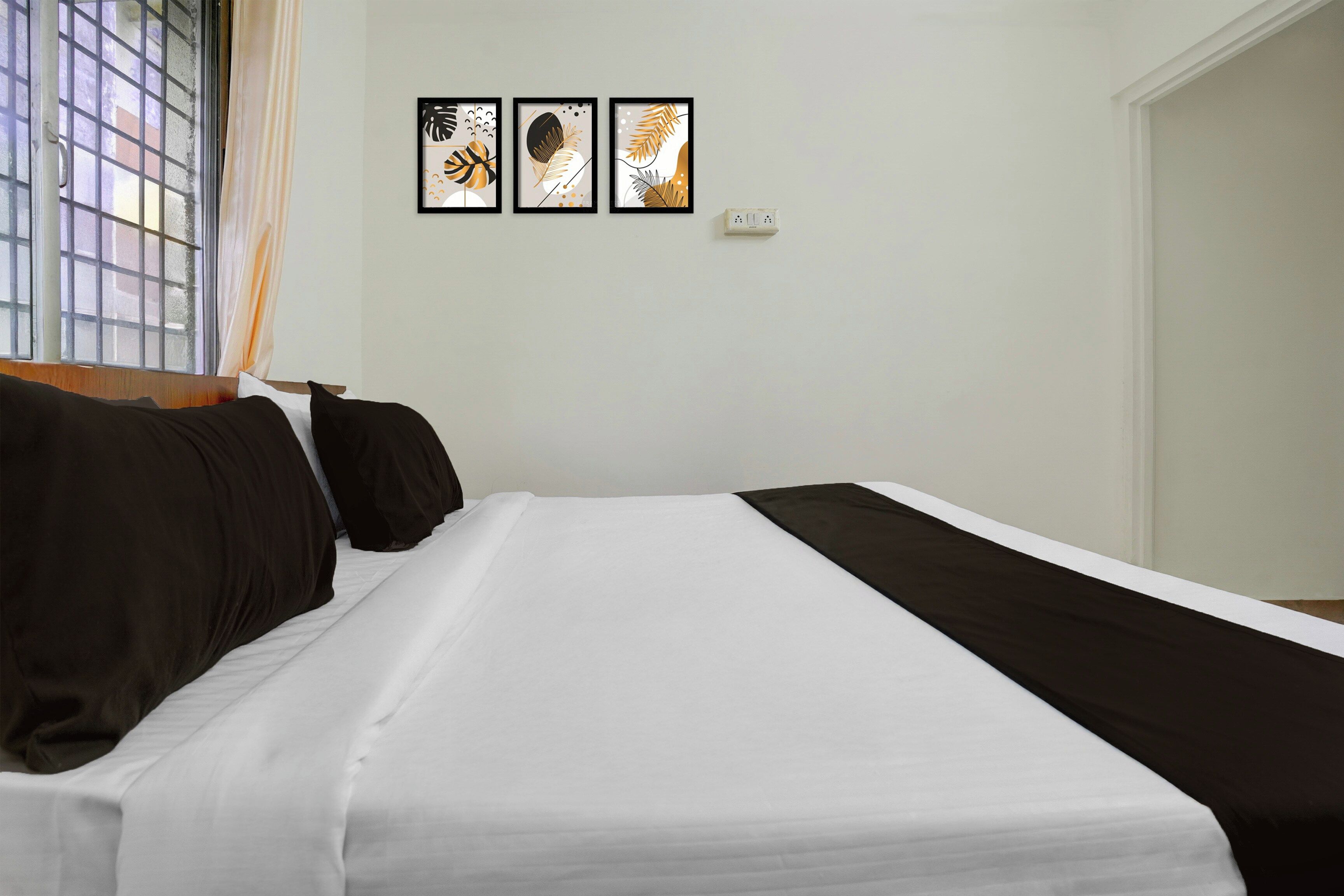 A hotel room with a bed, a window with a view, and three framed artworks on the wall.