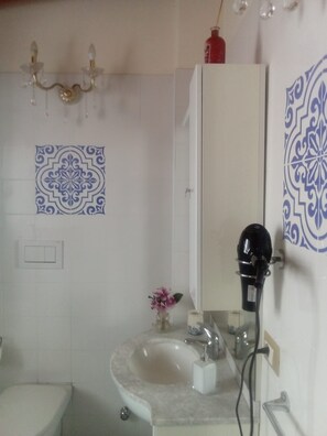 Casa de banho com uma pia branca, espelho e secador de cabelo no balcão.