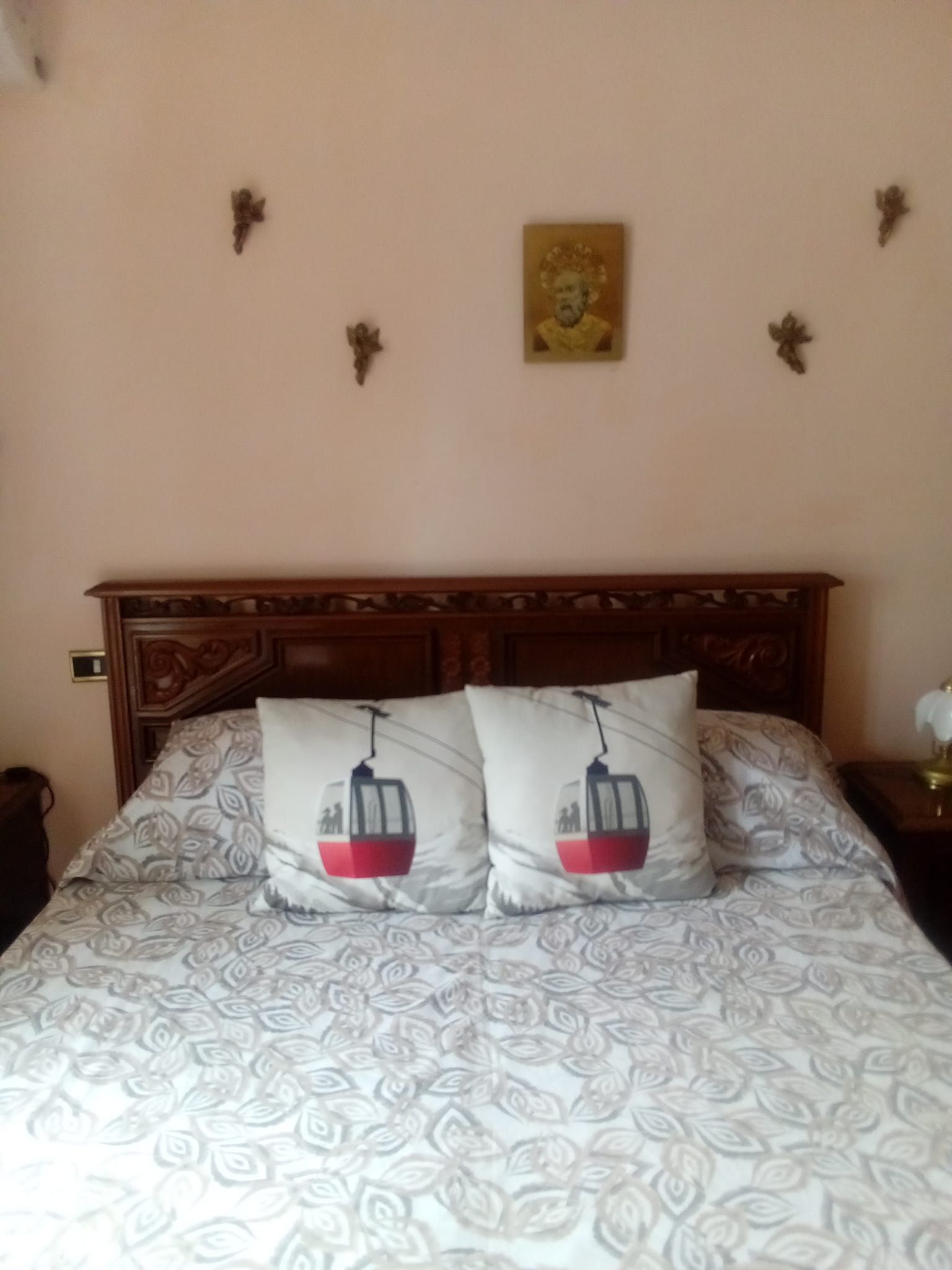 Ein Bett mit einem gemusterten Bettbezug und zwei Kissen mit einem Design von Seilbahnen, ein Holz-Kopfbrett und eine Wand mit einem gerahmten Bild und Wandleuchten.