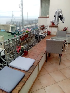 A balcony with a metal railing, potted plants, a table with chairs, and a view of the sea. - New Listing (Taormina)