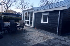 A patio area with a table and chairs, a covered seating area, and a building with a dark exterior and white trim. - Holiday apartment in Zoutelande with Wi-Fi (Zoutelande)