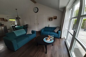 Een woonkamer met twee blauwgroene banken, een salontafel, een klok en een raam met uitzicht.