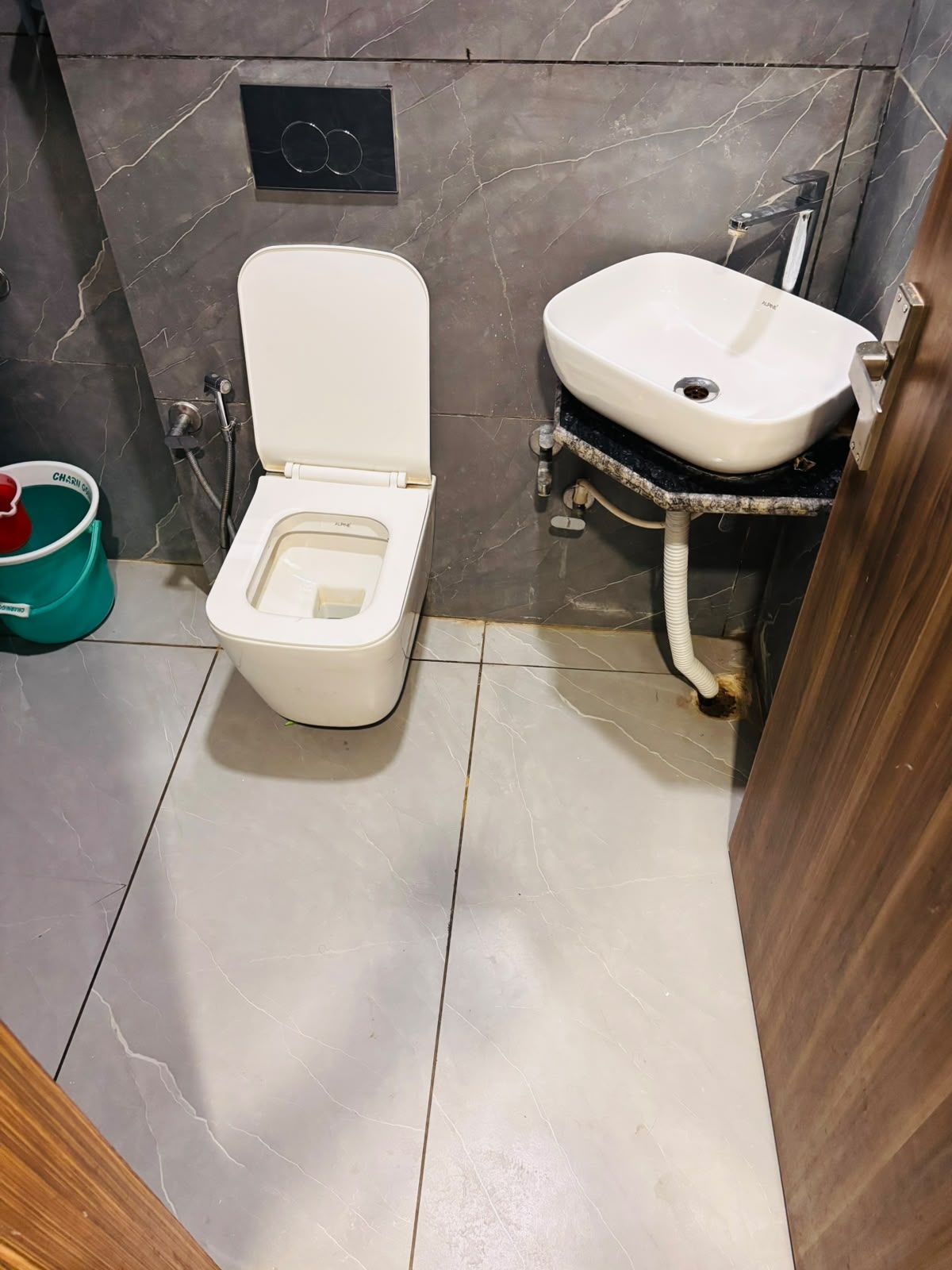 Une salle de bain avec des toilettes, un lavabo et un seau vert.
