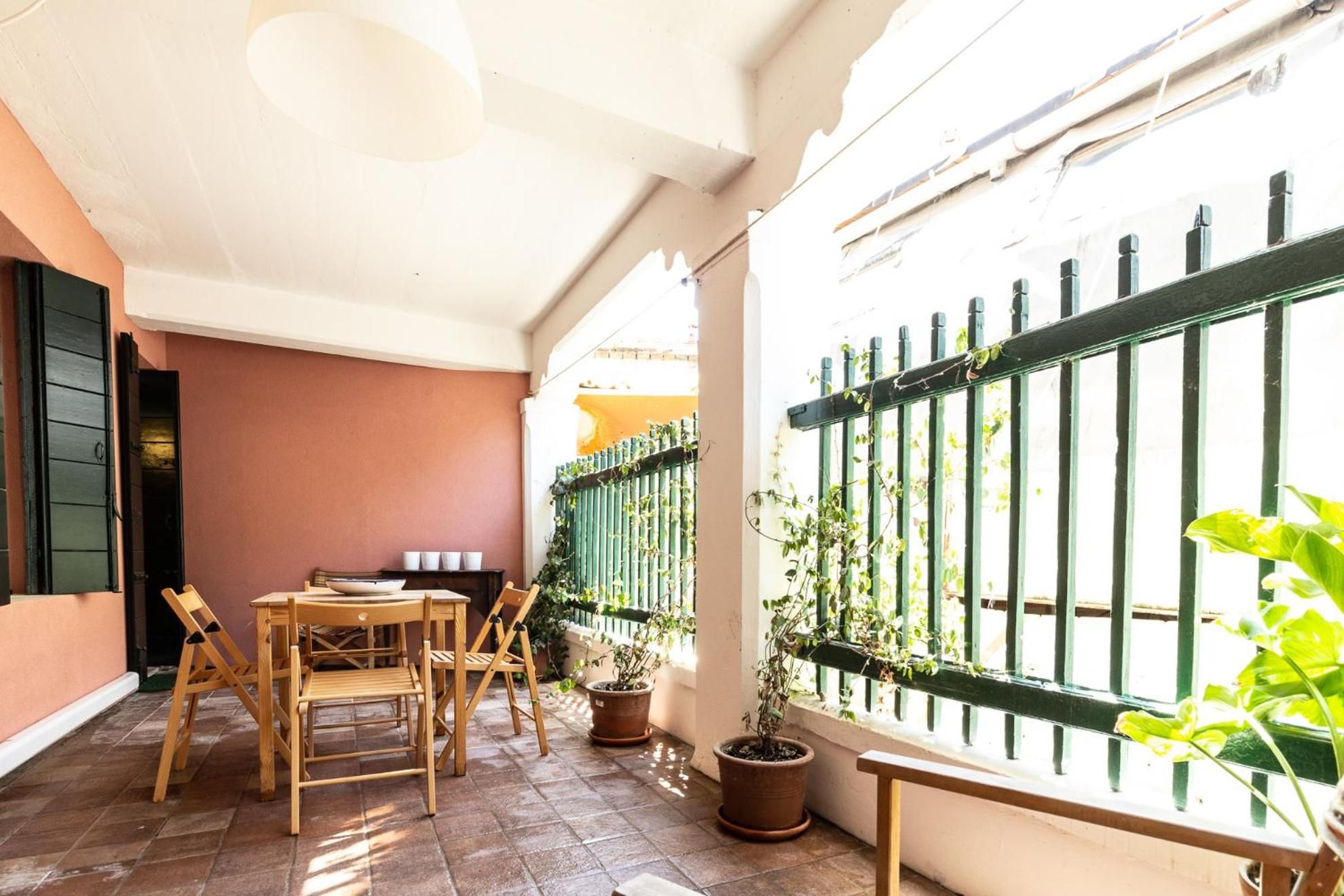 Un patio con una mesa y sillas, plantas en macetas y una cerca metálica verde.