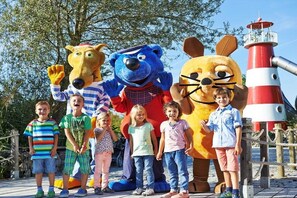 Een groep kinderen en twee grote mascottefiguren staan voor een vuurtoren.