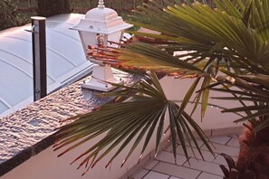 A white outdoor structure with a white lamp, a stone wall, and a palm tree. - Holiday apartment with 2 bedrooms (Meckenbeuren)