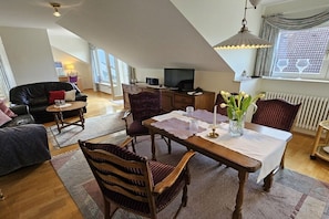 Ein gemütliches Wohnzimmer mit Esstisch, Stühlen, einer Couch und einem Fernseher.