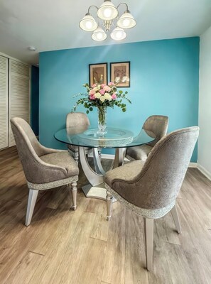 A dining area with a round glass table, four grey upholstered chairs, a vase with flowers, and a ceiling light fixture. - Wellington House - Deltona (Deltona)
