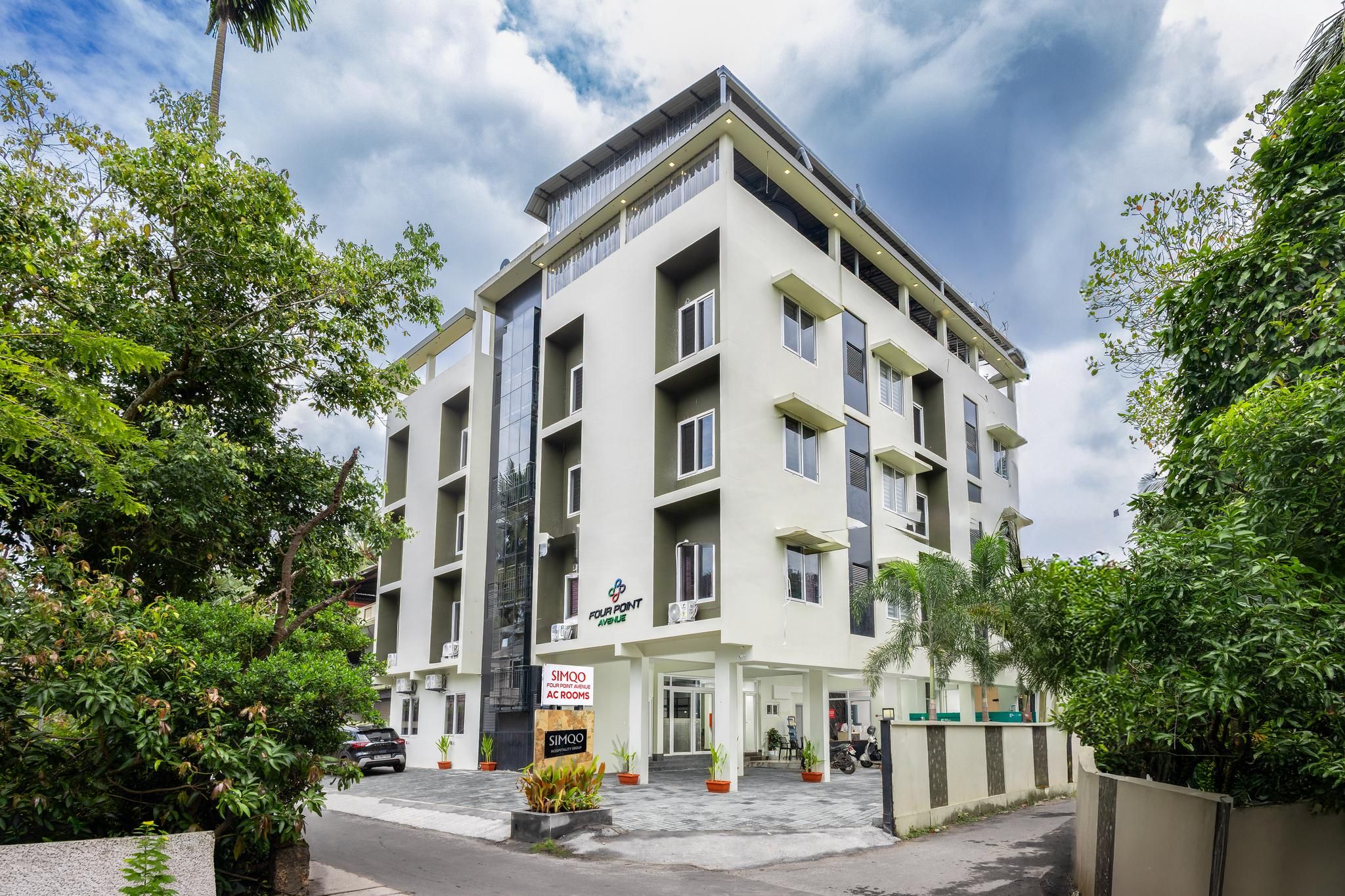 A multi-story hotel with a modern design, featuring balconies, air conditioning units, and a sign for 'SIMQO AC Rooms'.