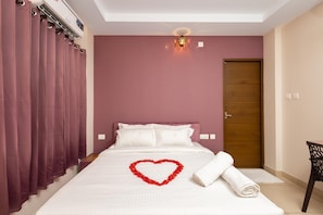 Una habitación de hotel con una cama, una decoración con forma de corazón en la cama, una puerta de madera y una silla.