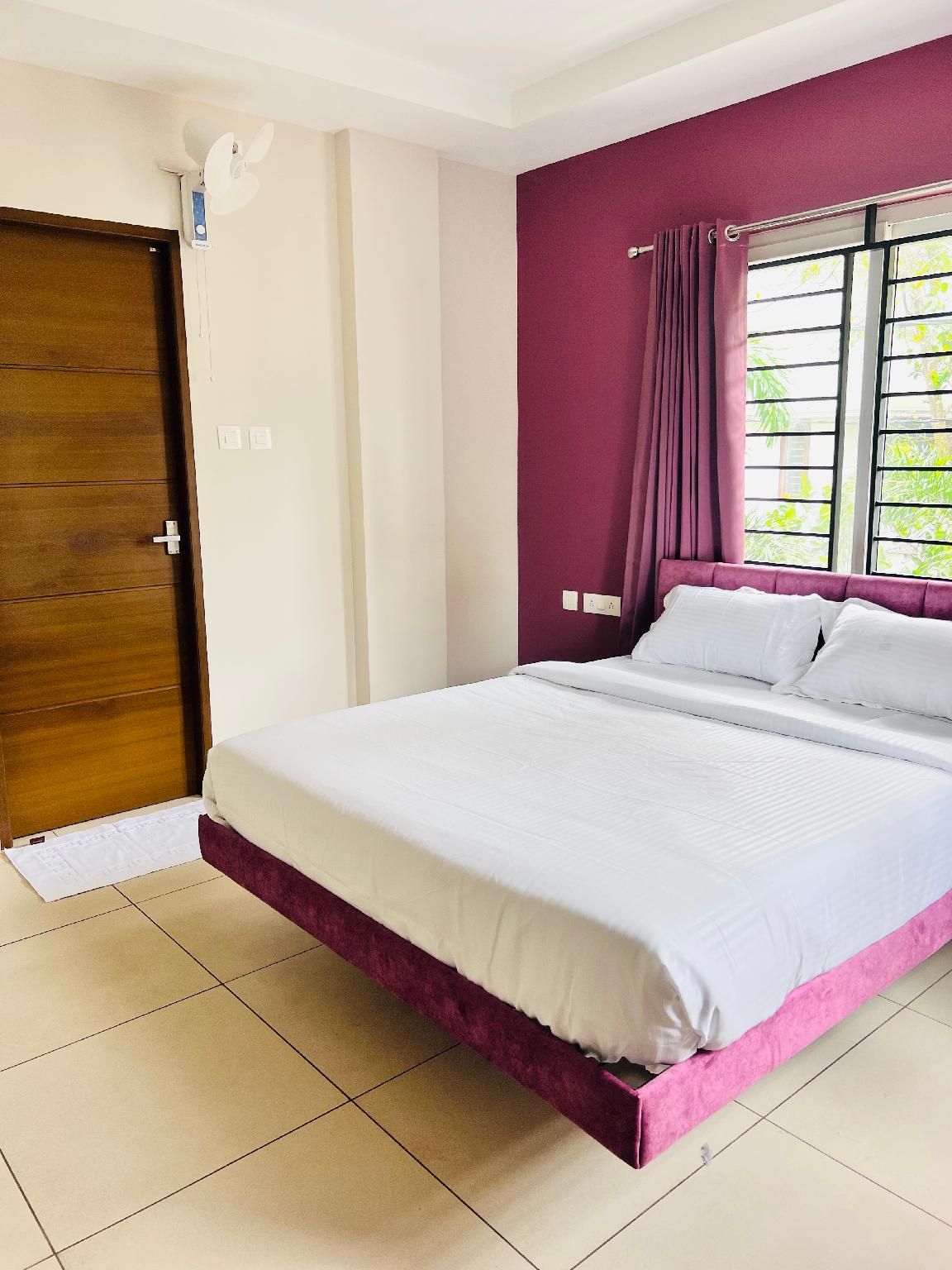 A bedroom with a bed, a window with curtains, a door, and a ceiling fan.
