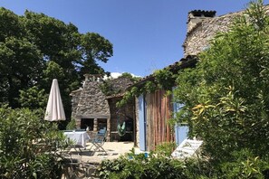 A stone building with a rustic exterior, a hanging chair, and a table set for outdoor dining. - Holiday home with 2 bedrooms (Lagorce, Ardèche)