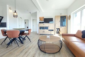 A modern living room with a round wooden coffee table, a leather sofa, and a dining area with a table and chairs. - Holiday apartment with 2 bedrooms (Lindau-Bodolz)