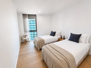 A hotel room with two beds, a chair, a nightstand, and a window with a view of a building. - Sky High at Sunrise - Lagoon Main Beach (Main Beach)
