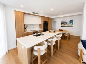 A modern kitchen with a central island, bar stools, and a dining table with chairs. - Sky High at Sunrise - Lagoon Main Beach (Main Beach)