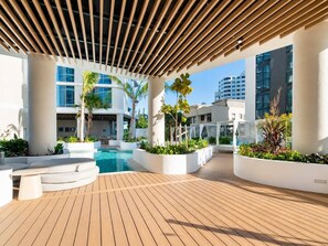 A modern outdoor pool area with a wooden deck, white planters with greenery, and a covered seating area. - Sky High at Sunrise - Lagoon Main Beach (Main Beach)
